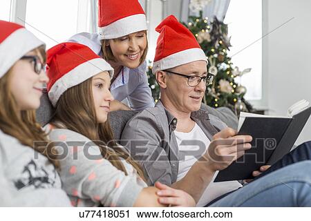 Stock Image - Father reading book for family at home during Christmas. Fotosearch