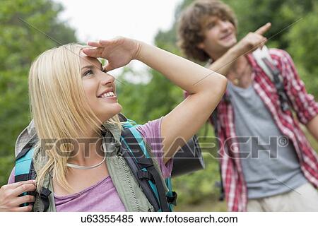 Stock Photography - Female backpacker looking away while man showing something in forest. Fotosearch