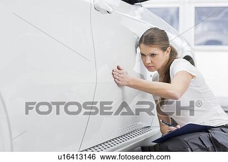 Stock Photograph - Female maintenance engineer examining car in workshop. Fotosearch