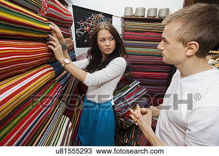 Stock Image - Female salesperson assisting man in textile store. Fotosearch