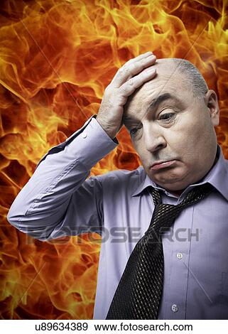Stock Photo - Frustrated businessman with hand on head standing against fire. Fotosearch