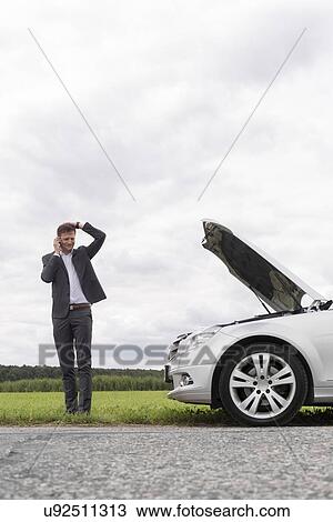 Frustrated young businessman using cell phone near broken down car at countryside View Large Photo Image Stock Image - Frustrated young businessman using cell phone near broken down car at countryside. Fotosearch