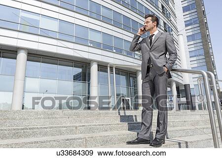 Full length businessman answering cell phone while standing on steps outside office View Large Photo Image Stock Photo - Full length businessman answering cell phone while standing on steps outside office. Fotosearch