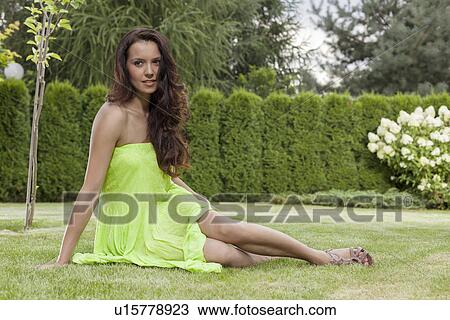 Stock Image - Full length of attractive young woman in sundress relaxing at park. Fotosearch