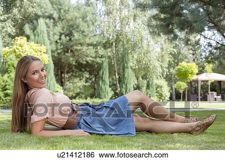 Full length of beautiful young woman reclining on grass in park View Large Photo Image Stock Photograph - Full length of beautiful young woman reclining on grass in park. Fotosearch