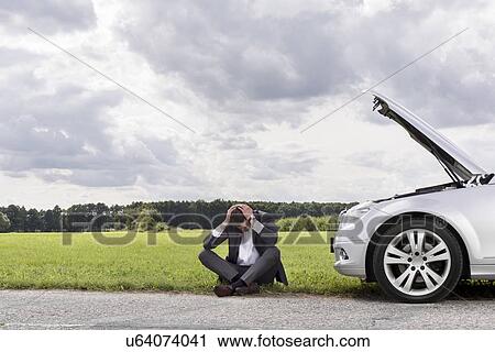 Full length of businessman with hands on head sitting by broken down car at countryside View Large Photo Image Stock Image - Full length of businessman with hands on head sitting by broken down car at countryside. Fotosearch