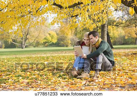 Stock Image - Full length of couple using tablet PC in park during autumn. Fotosearch