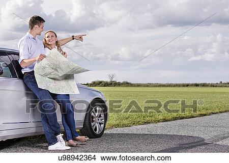 Full length of couple with map discussing direction while leaning on car at countryside View Large Photo Image Picture - Full length of couple with map discussing direction while leaning on car at countryside. Fotosearch