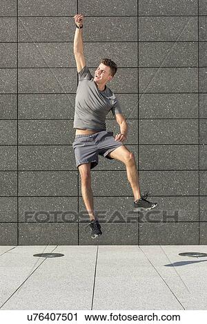 Stock Image - Full length of excited jogger jumping against tiled wall. Fotosearch