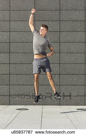 Full length of excited runner jumping against tiled wall View Large Photo Image Stock Photo - Full length of excited runner jumping against tiled wall. Fotosearch