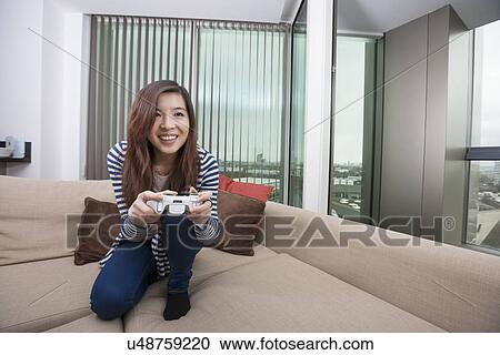 Full length of happy young woman playing video game on sofa at home View Large Photo Image Stock Image - Full length of happy young woman playing video game on sofa at home. Fotosearch
