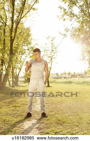 Full length of jogger listening music through cell phone in park View Large Photo Image Stock Photography - Full length of jogger listening music through cell phone in park. Fotosearch