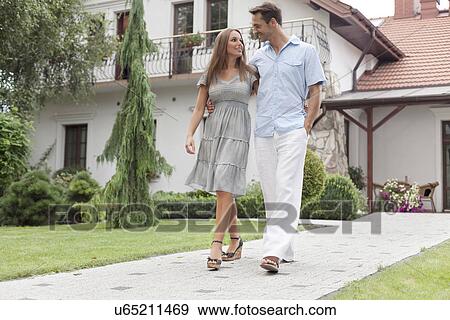 Stock Photo - Full length of loving young couple walking on footpath in park. Fotosearch