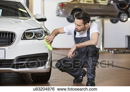 Stock Photograph - Full length of maintenance engineer cleaning car in workshop. Fotosearch