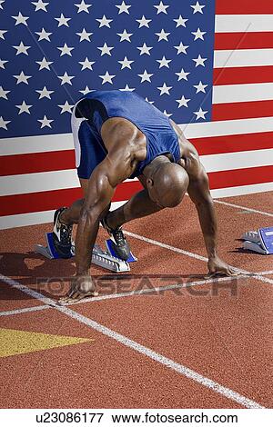 Stock Photo - Full length of male athlete ready to race with American flag in background. Fotosearch