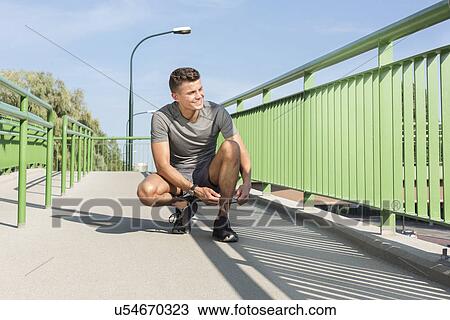 Full length of male jogger tying shoelace on bridge View Large Photo Image Stock Image - Full length of male jogger tying shoelace on bridge. Fotosearch