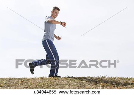 Stock Photography - Full length of man checking time while jogging against sky. Fotosearch