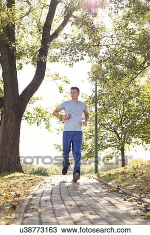 Full length of man listening music while jogging on path in park View Large Photo Image Stock Image - Full length of man listening music while jogging on path in park. Fotosearch