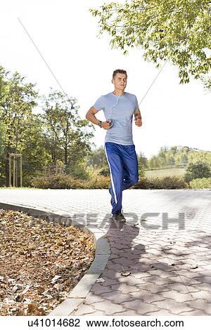 Stock Image - Full length of man listening music while jogging in park. Fotosearch