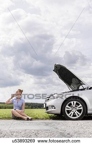 Full length of mid adult businesswoman on call while sitting beside broken down car at countryside View Large Photo Image Stock Photo - Full length of mid adult businesswoman on call while sitting beside broken down car at countryside. Fotosearch