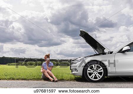 Full length of mid adult businesswoman on call while sitting beside broken down car at countryside View Large Photo Image Stock Photo - Full length of mid adult businesswoman on call while sitting beside broken down car at countryside. Fotosearch