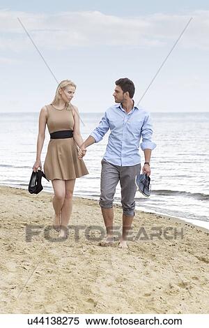 Full length of romantic young couple holding hands and walking on beach View Large Photo Image Stock Photography - Full length of romantic young couple holding hands and walking on beach. Fotosearch