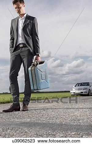 Full length of sad young businessman carrying petrol can with broken car in background at countryside View Large Photo Image Stock Image - Full length of sad young businessman carrying petrol can with broken car in background at countryside. Fotosearch