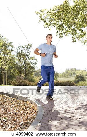 Full length of smiling man listening music while jogging in park View Large Photo Image Stock Image - Full length of smiling man listening music while jogging in park. Fotosearch