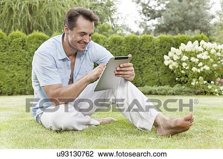 Full length of smiling young man using digital tablet in park View Large Photo Image Stock Image - Full length of smiling young man using digital tablet in park. Fotosearch