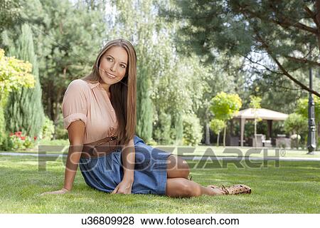 Full length of smiling young woman looking away while relaxing in park View Large Photo Image Stock Photo - Full length of smiling young woman looking away while relaxing in park. Fotosearch