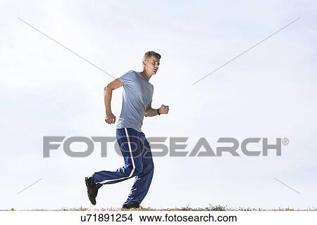 Picture - Full length of sporty man jogging against sky. Fotosearch