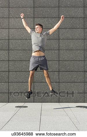 Stock Photo - Full length of successful jogger jumping against tiled wall. Fotosearch