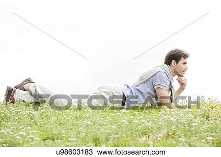 Full length of thoughtful young man lying on grass against clear sky View Large Photo Image Stock Image - Full length of thoughtful young man lying on grass against clear sky. Fotosearch