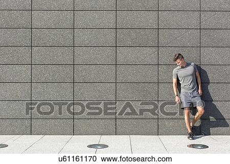 Stock Image - Full length of tired sporty man leaning on tiled wall. Fotosearch