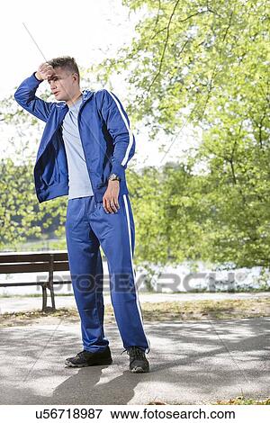 Stock Photo - Full length of tired young jogger standing on path in park. Fotosearch