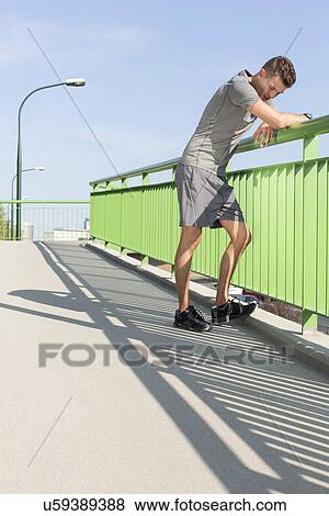 Full length of tired young man leaning on railing after jogging View Large Photo Image Stock Photo - Full length of tired young man leaning on railing after jogging. Fotosearch