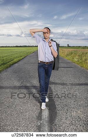 Full length of tired young man walking alone on rural road View Large Photo Image Picture - Full length of tired young man walking alone on rural road. Fotosearch