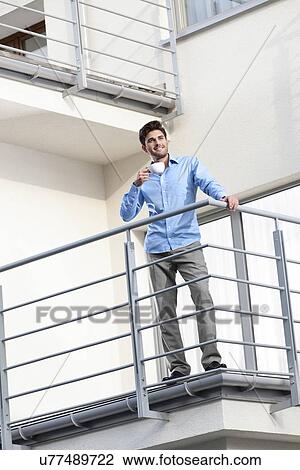Stock Image - Full length of young businessman having coffee at hotel balcony. Fotosearch