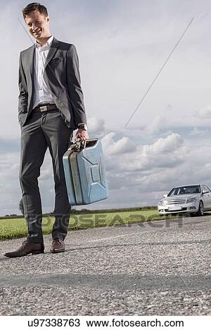 Full length of young businessman carrying gas can with broken down car in background at countryside View Large Photo Image Stock Image - Full length of young businessman carrying gas can with broken down car in background at countryside. Fotosearch