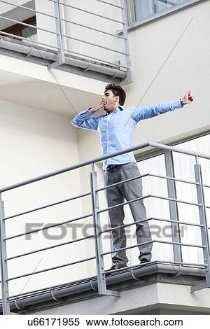 Stock Photography - Full length of young businessman stretching at hotel balcony. Fotosearch