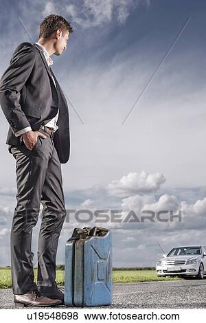Full length of young businessman with petrol can looking at broken car at countryside View Large Photo Image Stock Photo - Full length of young businessman with petrol can looking at broken car at countryside. Fotosearch
