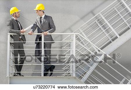 Picture - Full length of young male architect discussing on stairway. Fotosearch
