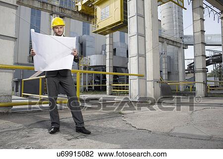 Full length of young male architect examining blueprint outside industry View Large Photo Image Stock Image - Full length of young male architect examining blueprint outside industry. Fotosearch