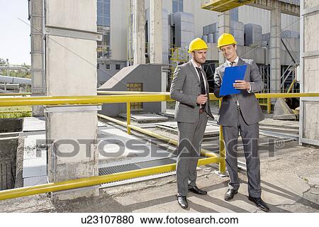 Full length of young male architects looking at clipboard on construction site View Large Photo Image Stock Image - Full length of young male architects looking at clipboard on construction site. Fotosearch