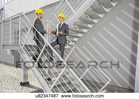 Stock Photo - Full length of young male architects discussing on steps. Fotosearch