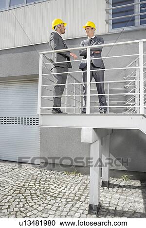 Stock Image - Full length of young male engineers discussing on stairway. Fotosearch