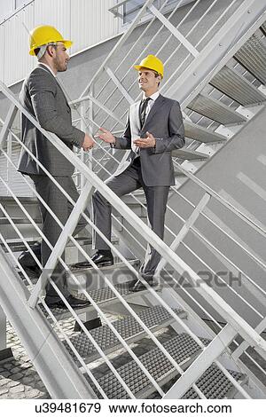 Stock Photo - Full length of young male engineers discussing on steps. Fotosearch