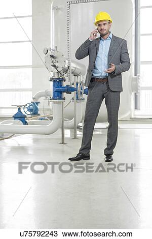 Stock Image - Full length of young male manager using cell phone in industry. Fotosearch