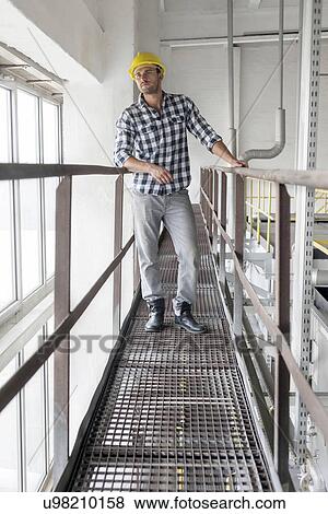 Full length of young male worker standing on metal aisle in industry View Large Photo Image Stock Photo - Full length of young male worker standing on metal aisle in industry. Fotosearch