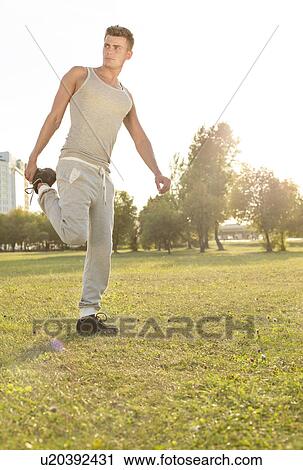 Stock Image - Full length of young man exercising in park. Fotosearch